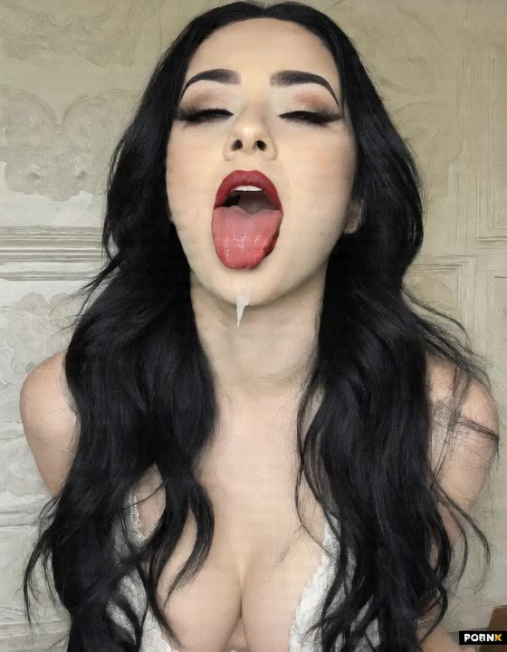 The woman maintains the same facial expression as cum sprays over her face